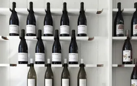 Étagères minimalistes avec des bouteilles de vin exposées dans un espace épuré. La présentation met en avant des vins rouges et blancs dans un décor moderne et lumineux, soulignant l'élégance et la simplicité d'une cave ou boutique spécialisée.